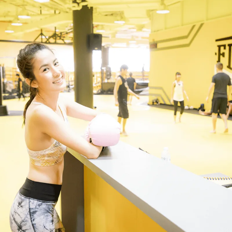 ผู้หญิงสวมนวมยืนพิงเคาน์เตอร์ ด้านหลังเป็นพื้นที่ฝึก — FITFAC สาขาเอกมัย