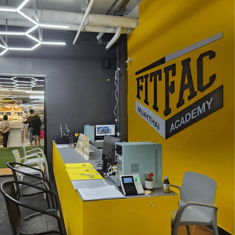 เคาน์เตอร์ต้อนรับข้างผนังโลโก้ FITFAC มองเห็นห้างผ่านทางเข้า — FITFAC สาขาเลียบด่วน