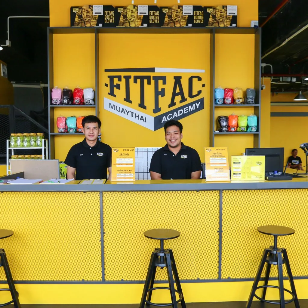 พนักงานสองคนที่เคาน์เตอร์ต้อนรับ หน้าชั้นวางนวม — FITFAC สาขาเมืองทองธานี