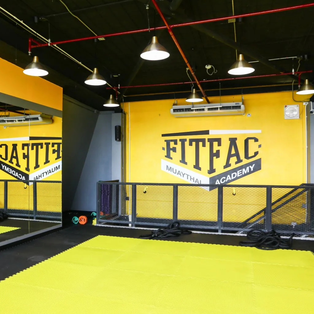 เบาะฝึกสีเหลืองกับผนังโลโก้ FITFAC ใต้โคมไฟแขวน — FITFAC สาขาเมืองทองธานี