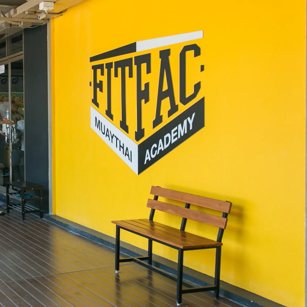 ม้านั่งใต้โลโก้ FITFAC Muaythai Academy บนผนังสีเหลือง — FITFAC สาขาราชพฤกษ์